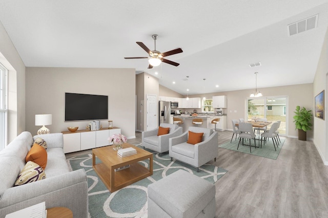 living room with light wood-type flooring, lofted ceiling, and ceiling fan with notable chandelier