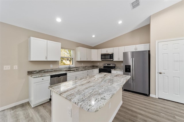 kitchen with lofted ceiling, a kitchen island, light stone countertops, appliances with stainless steel finishes, and white cabinets