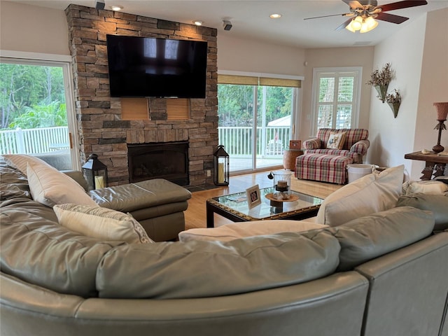 living room featuring hardwood / wood-style flooring, ceiling fan, and a stone fireplace