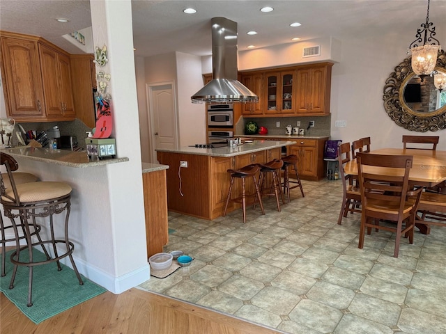 kitchen featuring pendant lighting, a breakfast bar area, tasteful backsplash, kitchen peninsula, and island exhaust hood