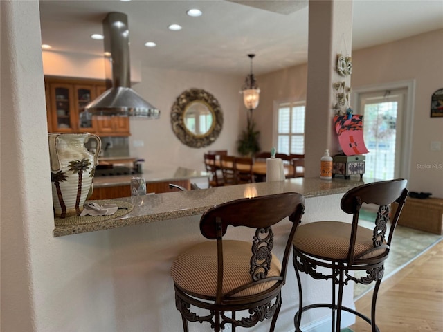 kitchen featuring island exhaust hood, light stone countertops, kitchen peninsula, and pendant lighting