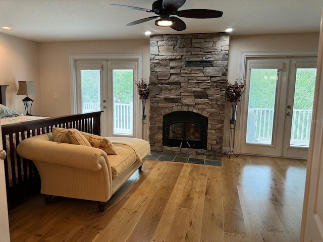 living room with hardwood / wood-style flooring, ceiling fan, and a stone fireplace