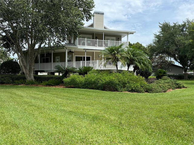 back of property with a yard, a balcony, and ceiling fan