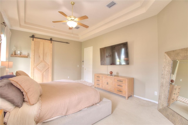 bedroom featuring a tray ceiling, light colored carpet, a barn door, and ceiling fan