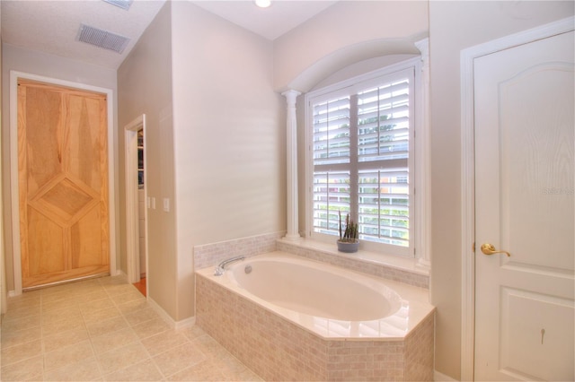 bathroom with tile patterned flooring, plenty of natural light, a relaxing tiled tub, and ornate columns