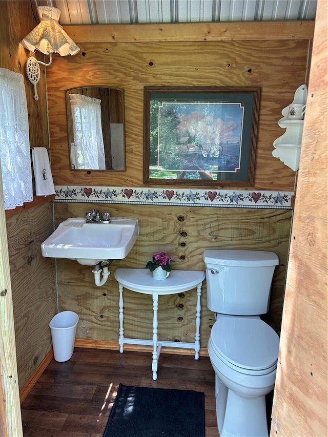 bathroom featuring wood walls, wood-type flooring, toilet, and sink