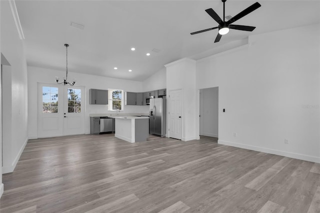 unfurnished living room with ceiling fan with notable chandelier, high vaulted ceiling, and light wood-type flooring