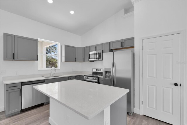 kitchen with a center island, light hardwood / wood-style floors, sink, vaulted ceiling, and appliances with stainless steel finishes