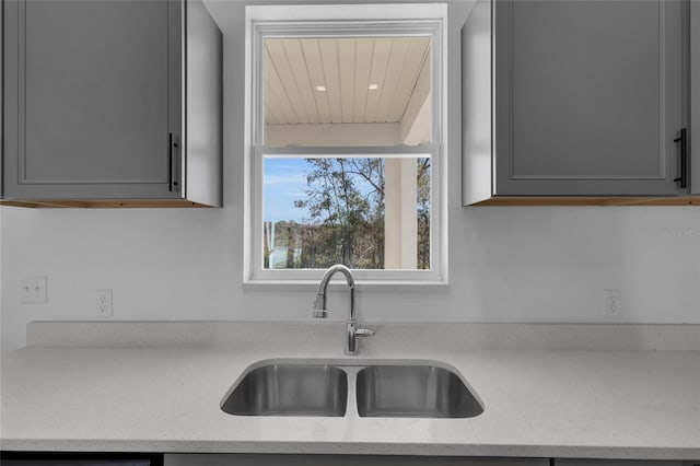 kitchen featuring dishwashing machine, sink, gray cabinetry, and light stone countertops