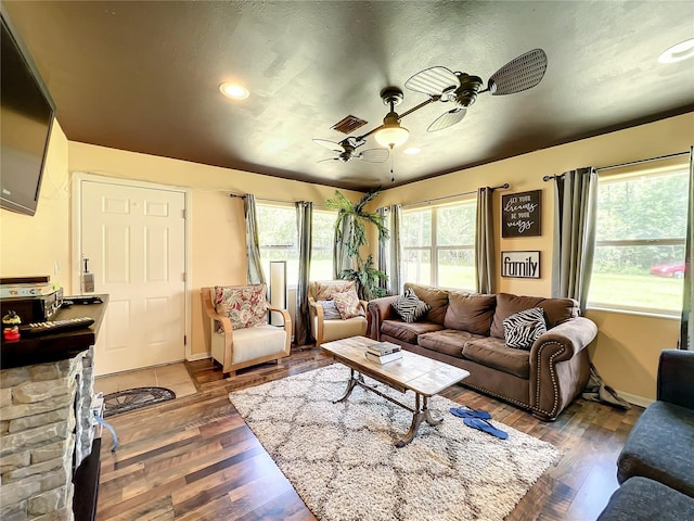 living room featuring dark hardwood / wood-style floors, a stone fireplace, and ceiling fan