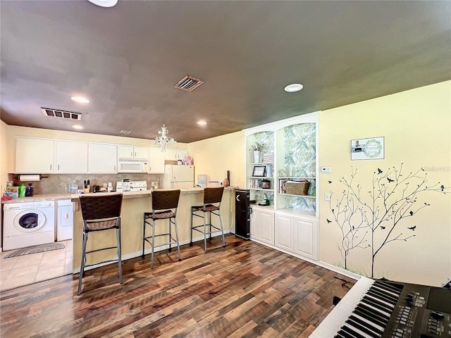 kitchen with a breakfast bar, separate washer and dryer, backsplash, white cabinets, and white appliances