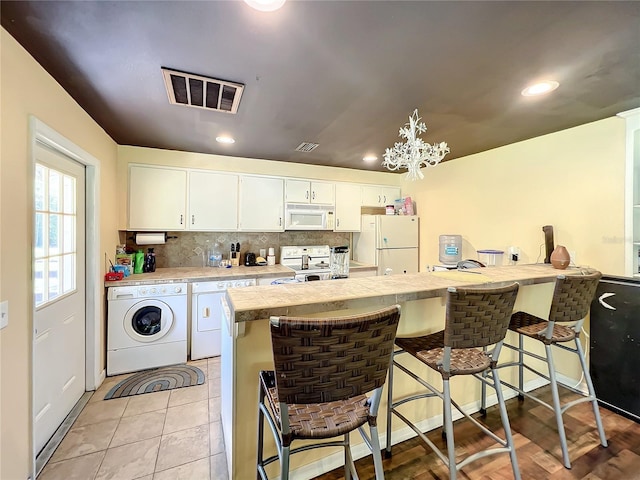 kitchen featuring washing machine and clothes dryer, white cabinets, and white appliances