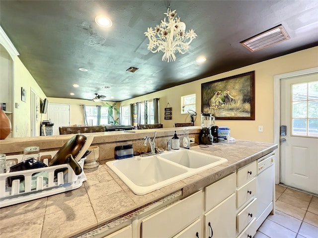 kitchen featuring sink, light tile patterned floors, white cabinetry, white dishwasher, and tile countertops