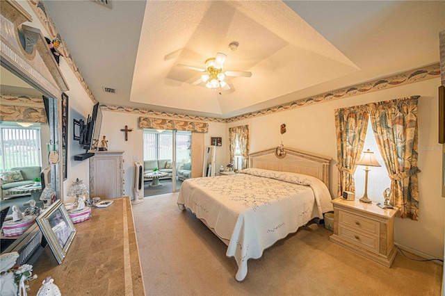 bedroom with a textured ceiling, light colored carpet, a raised ceiling, and ceiling fan