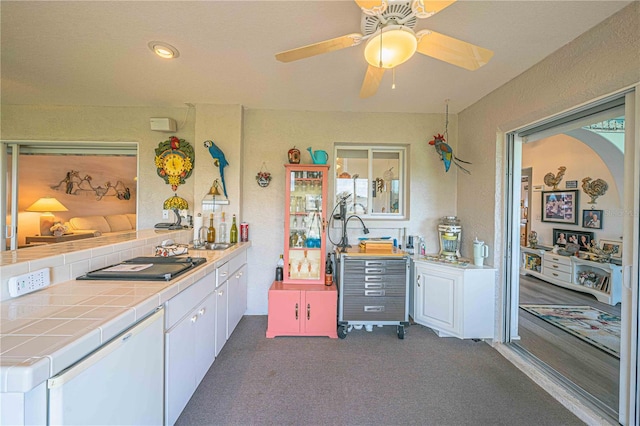 kitchen featuring dark carpet, stainless steel gas cooktop, sink, white cabinetry, and tile counters