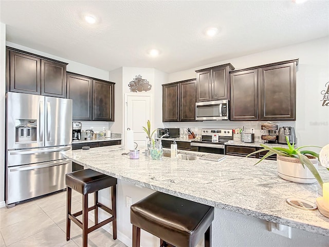 kitchen with sink, a breakfast bar area, light tile patterned floors, dark brown cabinets, and stainless steel appliances