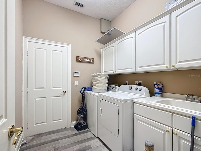 laundry area featuring sink, cabinets, independent washer and dryer, light hardwood / wood-style floors, and a textured ceiling