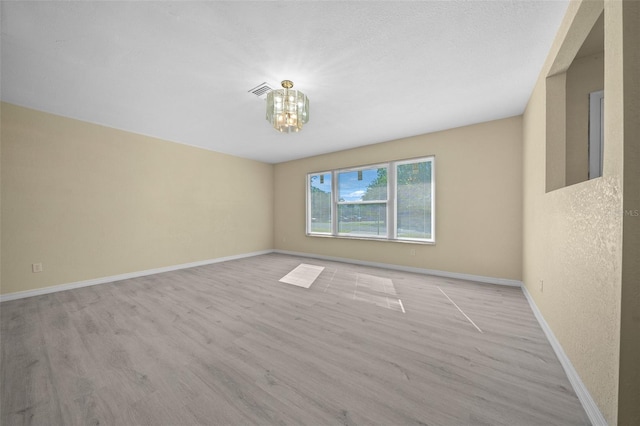 empty room with a chandelier and light wood-type flooring