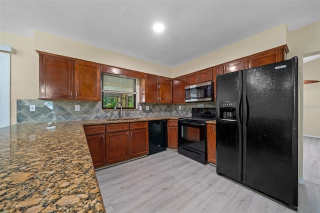 kitchen with sink, stone countertops, decorative backsplash, black appliances, and light wood-type flooring