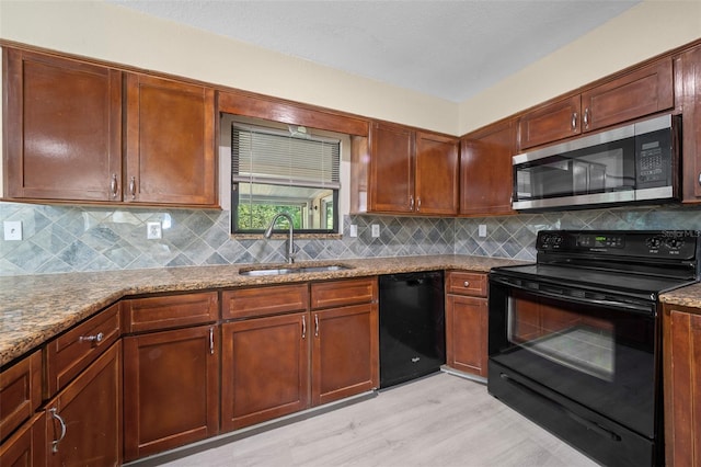 kitchen with light stone countertops, decorative backsplash, sink, and black appliances