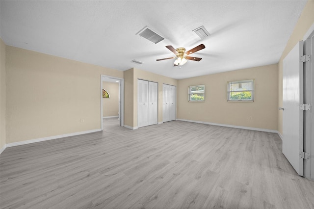 unfurnished bedroom featuring a textured ceiling, ceiling fan, light hardwood / wood-style flooring, and two closets