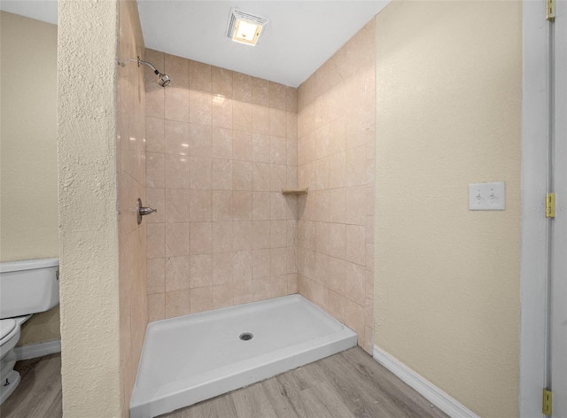 bathroom with hardwood / wood-style floors, a tile shower, and toilet