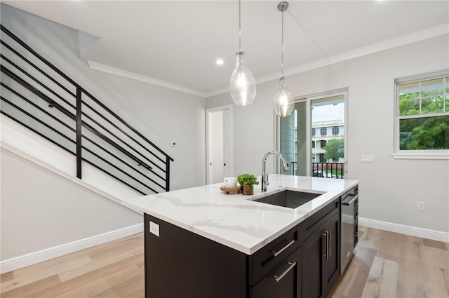 kitchen featuring dishwasher, sink, light stone counters, light hardwood / wood-style floors, and a center island with sink