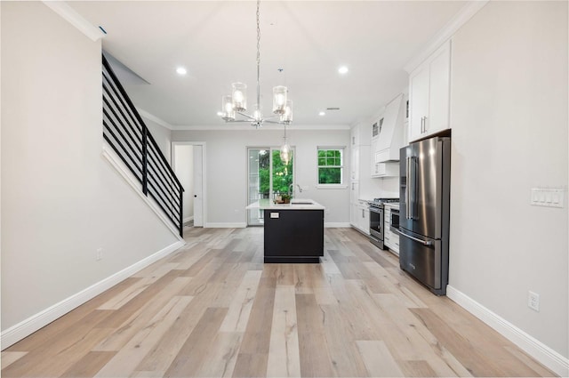 kitchen with a center island with sink, white cabinets, ornamental molding, appliances with stainless steel finishes, and decorative light fixtures