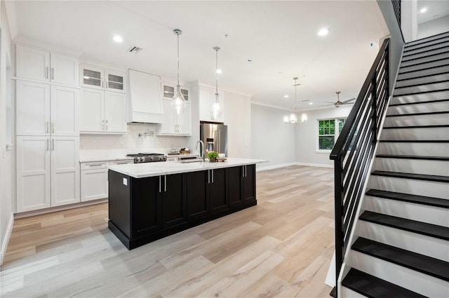 kitchen with pendant lighting, custom exhaust hood, a center island with sink, ceiling fan, and stainless steel fridge with ice dispenser