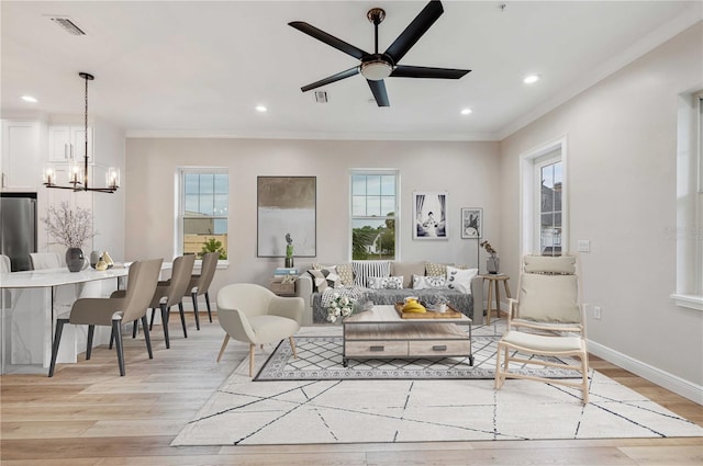 living room with ceiling fan with notable chandelier, light hardwood / wood-style floors, ornamental molding, and a wealth of natural light