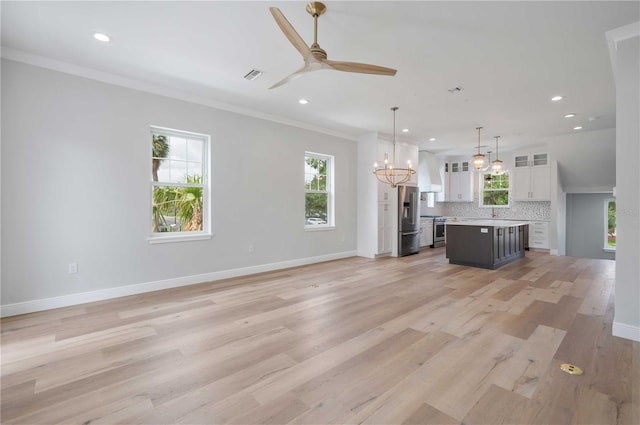 unfurnished living room featuring ceiling fan with notable chandelier, light hardwood / wood-style floors, and crown molding