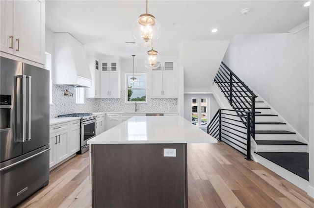 kitchen with high quality appliances, premium range hood, hanging light fixtures, light wood-type flooring, and white cabinetry