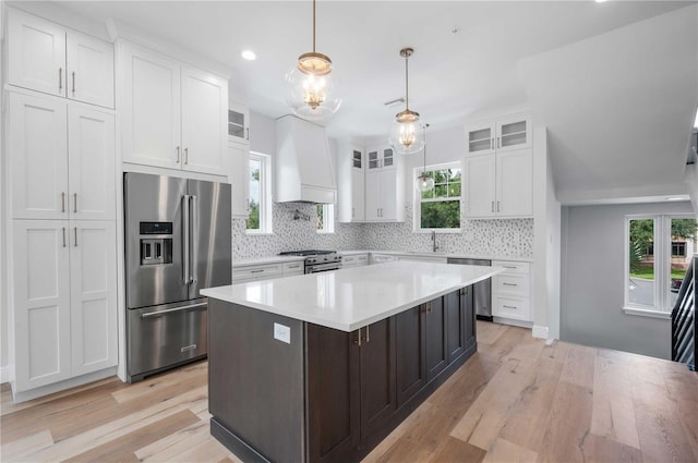 kitchen featuring high quality appliances, a kitchen island, custom range hood, light hardwood / wood-style floors, and white cabinetry