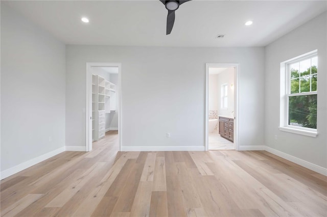 unfurnished bedroom featuring connected bathroom, ceiling fan, light hardwood / wood-style floors, a walk in closet, and a closet