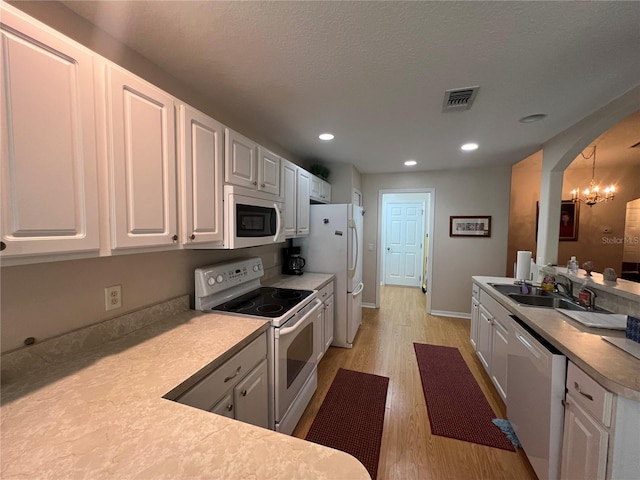 kitchen with white appliances, light wood-type flooring, white cabinets, hanging light fixtures, and sink