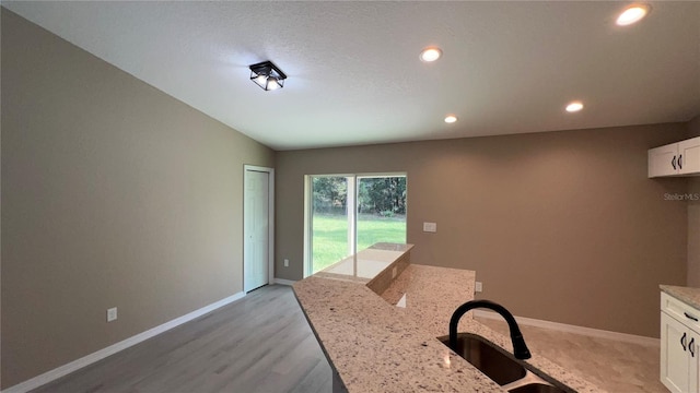 kitchen with vaulted ceiling, sink, white cabinets, light stone countertops, and light wood-type flooring