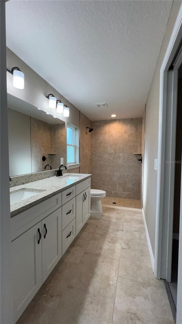 bathroom featuring vanity, toilet, a textured ceiling, and tiled shower