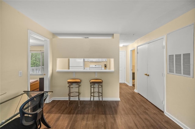 kitchen with white appliances, a breakfast bar area, and dark wood-type flooring