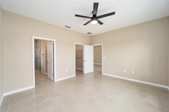 unfurnished bedroom with ensuite bathroom, ceiling fan, light tile patterned floors, a spacious closet, and a closet