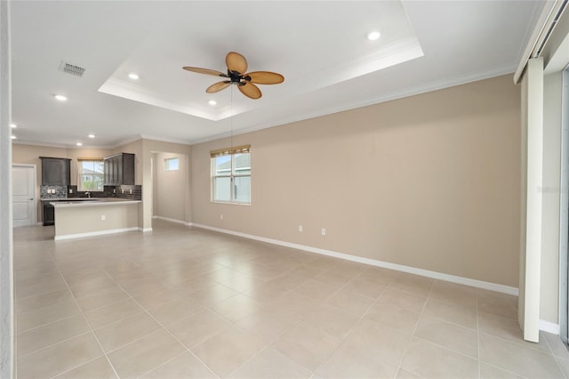 unfurnished living room featuring a wealth of natural light, a tray ceiling, ceiling fan, and crown molding