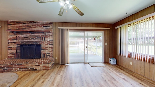 unfurnished living room featuring ceiling fan, light wood-type flooring, a fireplace, and wood walls