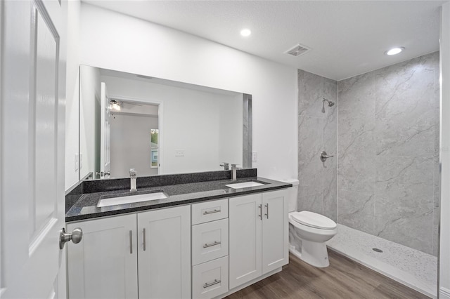 bathroom featuring hardwood / wood-style flooring, tiled shower, vanity, and toilet