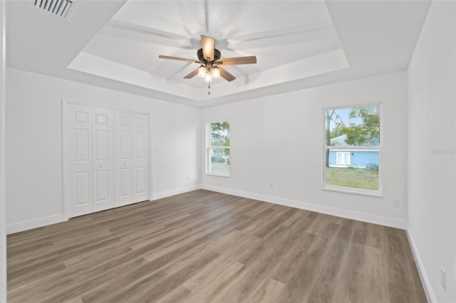 unfurnished bedroom featuring ceiling fan, a tray ceiling, and multiple windows