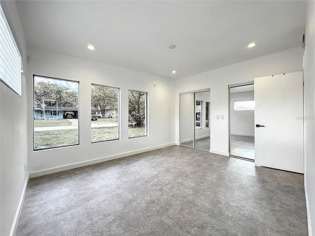 unfurnished bedroom featuring finished concrete flooring, recessed lighting, baseboards, and multiple closets