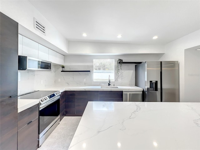 kitchen with light stone counters, a sink, appliances with stainless steel finishes, open shelves, and modern cabinets