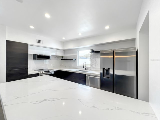 kitchen with modern cabinets, light stone counters, stainless steel appliances, white cabinetry, and a sink