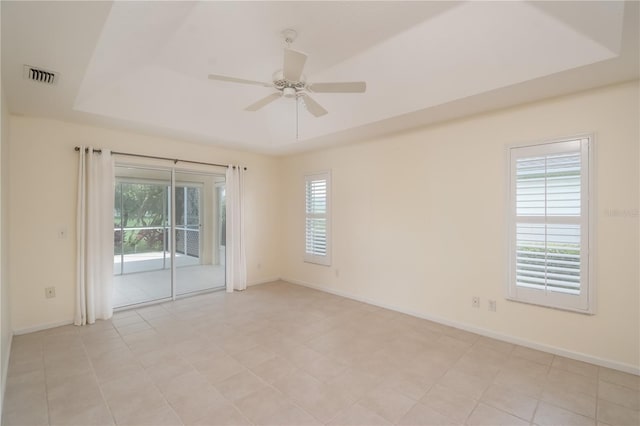 tiled spare room featuring a healthy amount of sunlight, ceiling fan, and a tray ceiling