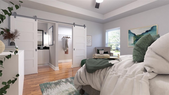 bedroom featuring a barn door, wood-type flooring, ceiling fan, and a tray ceiling