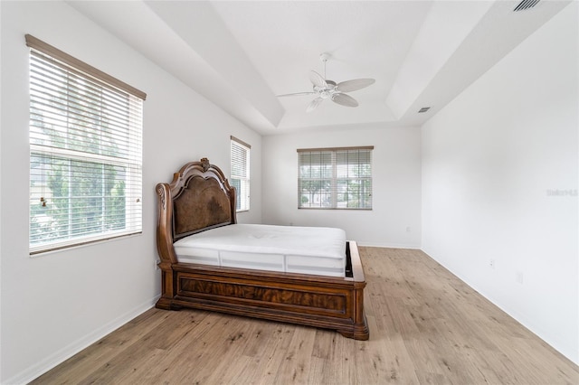 bedroom with a tray ceiling, ceiling fan, and light wood-type flooring