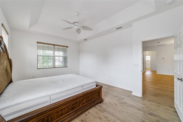 bedroom with a raised ceiling, ceiling fan, and light hardwood / wood-style floors